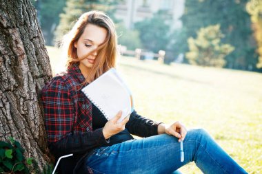 Ağacın yanındaki kız öğrenci dersin ve hayallerin başlamasını bekliyor.