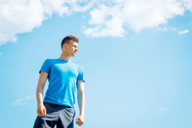 Genç ve neşeli sporcu güneşin altında gökyüzüne karşı