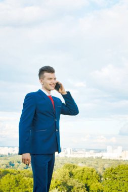 Mavi takım elbise ve kırmızı kravat takarak şehrin ve gökyüzünün zeminine karşı elinde bir evrak çantasıyla iyi bir anlaşma yapan neşeli güler yüzlü işadamı.