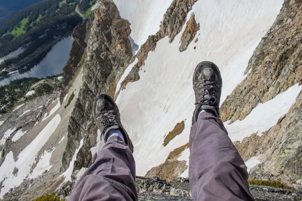 Ein Wanderer baumelt mit den Beinen über den Rand einer Klippe in den felsigen Bergen. — Stockfoto