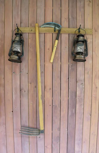 Традиционные сельскохозяйственные инструменты и масляная лампа на деревянной стене — стоковое фото