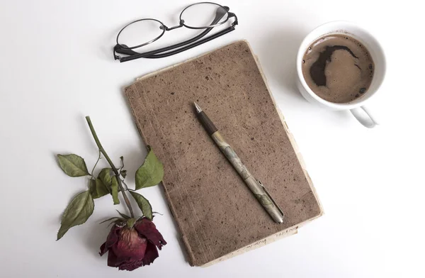 Σημειωματάριο, στυλό, φλιτζάνι καφέ και κόκκινο τριαντάφυλλο στο τραπέζι — Φωτογραφία Αρχείου