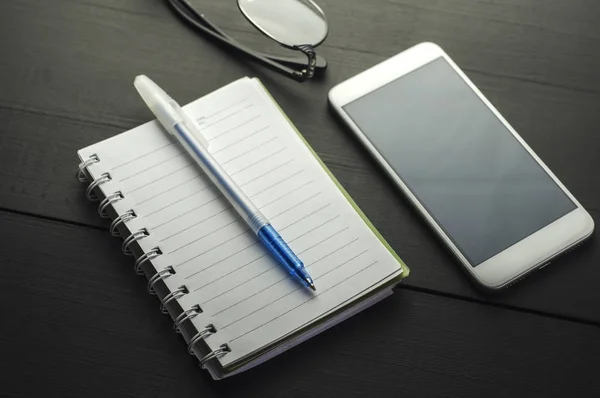 Smartphone και σημειωματάριο στο σκοτεινό ξύλινο τραπέζι — Φωτογραφία Αρχείου