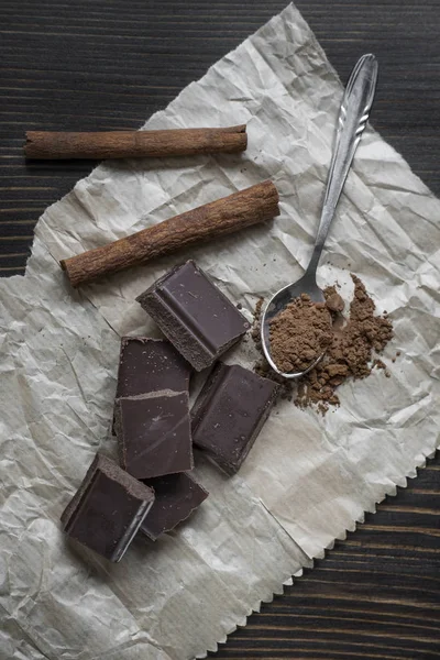 Broken chocolate bar and spices on wooden table. — Stock Photo, Image