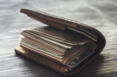 Ahşap arka planda para dolu eski deri cüzdan.