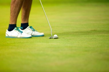 Golf topu ve arka planda golfçü bacakları ile sopa