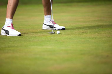 Golf topu ve arka planda golfçü bacakları ile sopa