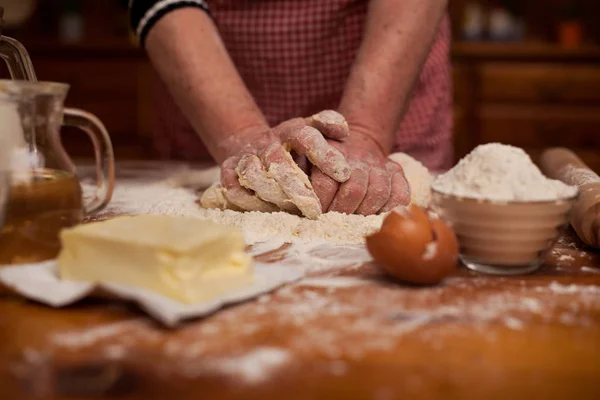 Las manos ancianas amasan la masa en la mesa en la cocina casera —  Fotos de Stock