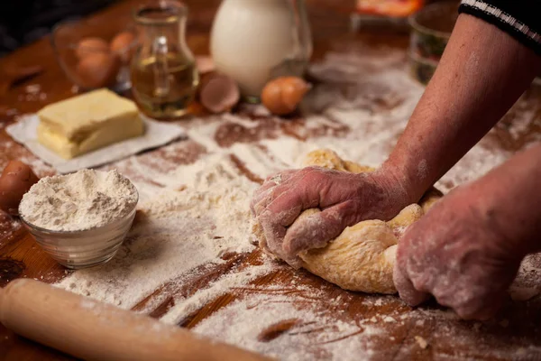 Las manos ancianas amasan la masa en la mesa en la cocina casera —  Fotos de Stock