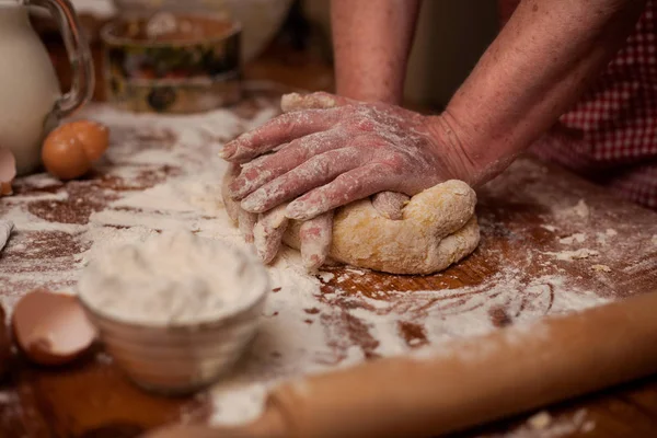 Руки старшої жінки замішують тісто на столі на домашній кухні — стокове фото