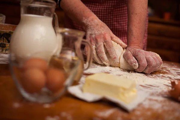 Starší žena rukou Uhněteme těsto na stole v domácí kuchyni — Stock fotografie