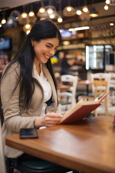 美丽的女人有喝咖啡的休息时间，阅读本书在咖啡馆 免版税图库图片