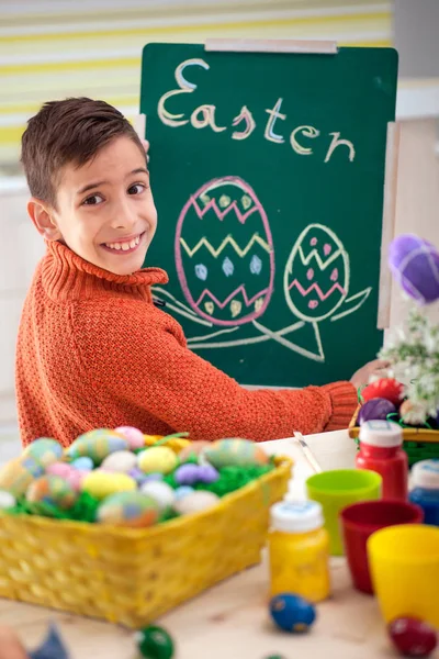 Usměvavý chlapec kreslí velikonoční vajíčka s křídou na zelenou tabuli — Stock fotografie