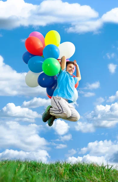 Feliz niño saltar en el prado con globos de colores contra azul sk —  Fotos de Stock