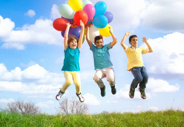 Happy smiling group of kids jumping with balloons on a green mea — Stock Photo, Image