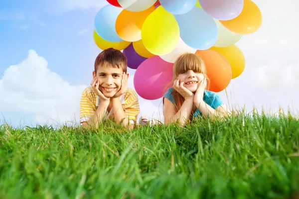 Niños sonrientes felices acostados en la hierba verde con colorfull b —  Fotos de Stock