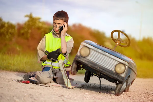 Divertido chico con coche juguete llamando desde el teléfono móvil asistencia en carretera — Foto de Stock