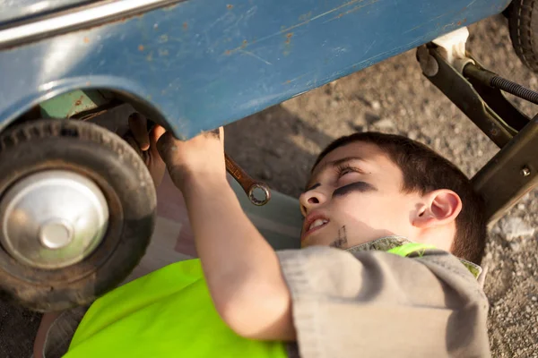 Jovem rapaz trocando um pneu em um carro de brinquedo velho — Fotografia de Stock