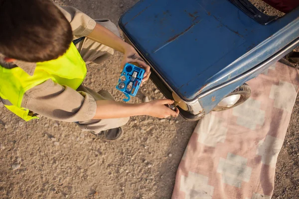 Boy changing light bulbs on his retro toy car — Stock Photo, Image