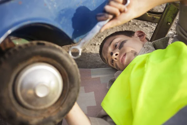 Chico joven cambiando un neumático en un coche de juguete viejo — Foto de Stock