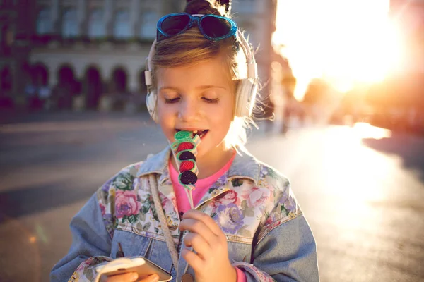 Little girl  listening  music  and eating  fruit lollipop,beauti — Stock Photo, Image