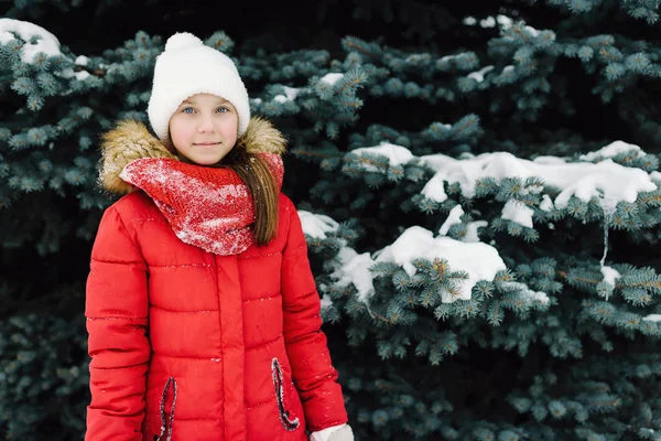 Portret van een meisje in een rode jas, in de buurt van de groene boom op straat — Stockfoto