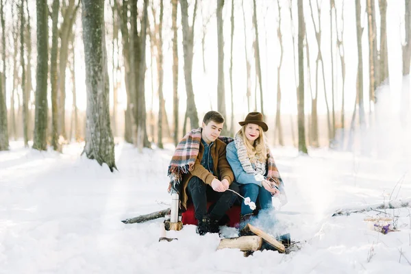 Jeune couple élégamment habillé, assis près du feu dans la forêt d'hiver — Photo