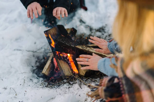Stylově oblečený mladý pár, sedí u ohně v zimním lese — Stock fotografie