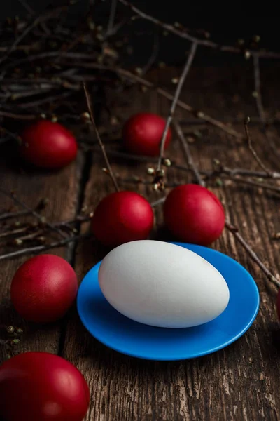 Easter eggs of red color on a wooden background, together with autumn branches