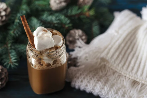 Cappuccino Tahun Baru dengan marshmallow, syal rajutan putih di atas meja kayu biru tua, untuk dekorasi, pinus untuk cabang dengan kerucut — Stok Foto