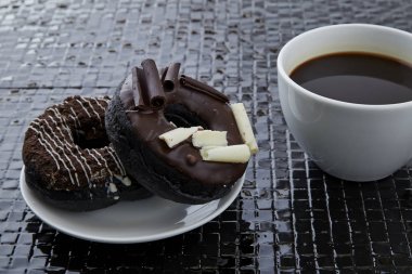 Siyah seramik zemin üzerinde siyah kahve fincan çikolatalı çörek