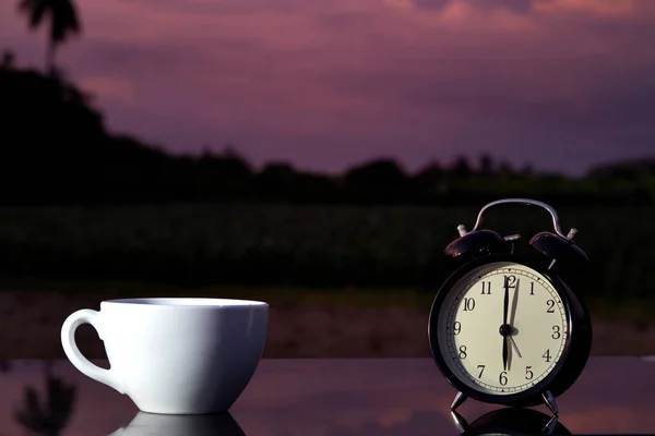 Orologio a campana nero e tazza di caffè caldo sul tavolo in legno in giardino — Foto Stock