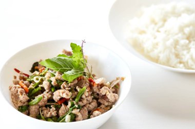 Beyaz ahşap zemin üzerinde masada kızarmış domuz tabak içinde fesleğen ve pirinç plaka ile karıştırın. Tayland gıda