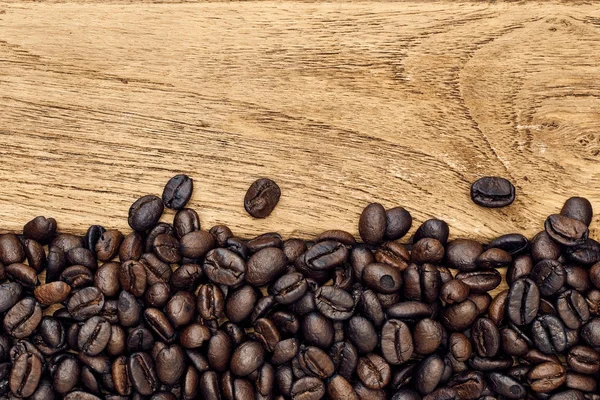 Black coffee grains lie on a brown wooden table, background