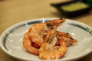 Ahşap masa üzerinde bir tabak içinde pişmiş bütün karides hizmet