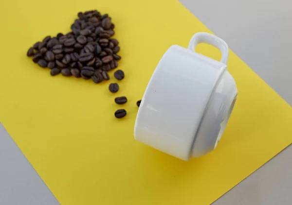 黄色の背景の上に白いカップとハートの形のコーヒー豆 バレンタイン コンセプト — ストック写真