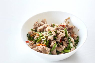 Beyaz ahşap zemin üzerinde masada kızarmış domuz tabak içinde fesleğen ve pirinç plaka ile karıştırın. Tayland gıda