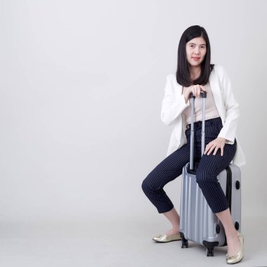 Güzel, genç Asyalı turist gülümseyen ve gri renkli bavul çeken turist seyahati için izole edilmiş açık gri stüdyo arkaplanında fotokopi alanı olan.