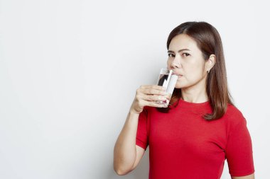 Genç gülümseyen Asyalı kadın beyaz arka planda izole edilmiş cam bir stüdyo resminden su içiyor, saf su konsepti ve sağlık hizmeti.