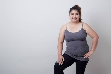 Güzel, modaya uygun, şişman, egzersiz elbiseli, gri arka planda duran, sağlıklı egzersiz konsepti olan Asyalı kadın.