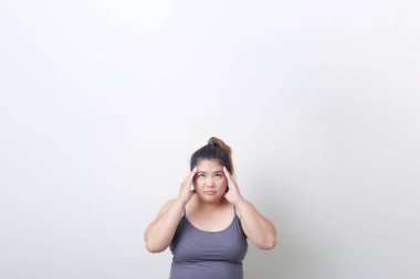 Güzel, modaya uygun, tombul, Asyalı kadın baş ağrısı. Parlak gri arka planda egzersiz kıyafetleri.