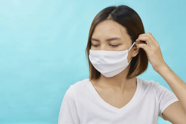 Asian woman with brown hair and a medical mask for protection again influenza on light blue background. Copy space for your text.  COVID-19 fighting concept.