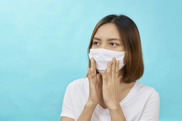 Asian woman with brown hair and a medical mask for protection again influenza on light blue background. Copy space for your text.  COVID-19 fighting concept.