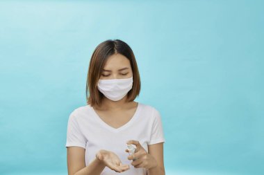 Genç Asyalı kadınlar koruyucu maskeler ve el dezenfektanı, koronavirüs enfeksiyonunu önlemek için alkol ve mavi arka plan bakterisi takıyorlar.