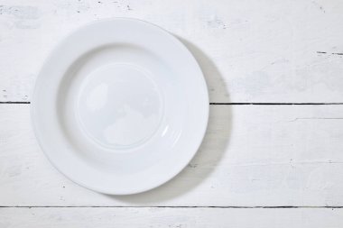 Beyaz tabak ve beyaz tahta masa zemininde fotokopi alanı olan beyaz tabağın üst görüntüsü. metin ve işaretlerle kullanmak için.