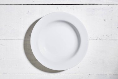 Beyaz tabak ve beyaz tahta masa zemininde fotokopi alanı olan beyaz tabağın üst görüntüsü. metin ve işaretlerle kullanmak için.