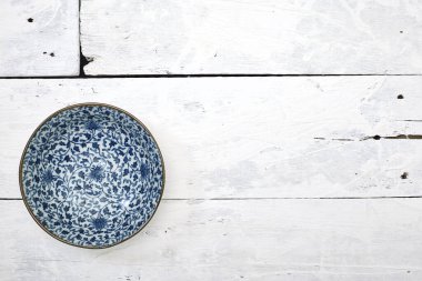 Düz uzanmış, beyaz ahşap masa üzerinde mavi desenli boş porselen tabaka.