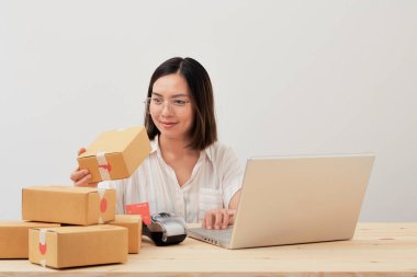 Mutlu Asyalı kadın karton kutuyla ev ambalajlama ve yazma sırası ile çalışıyor, online pazarlama paketleme ve teslimat, KOBİ kavramı
