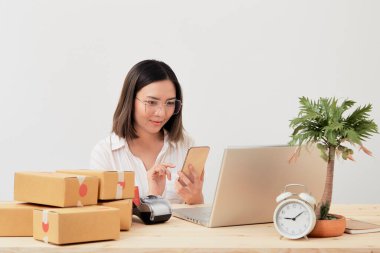 Mutlu Asyalı kadın karton kutuyla ev ambalajlama ve yazma sırası ile çalışıyor, online pazarlama paketleme ve teslimat, KOBİ kavramı