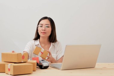 Mutlu Asyalı kadın karton kutuyla ev ambalajlama ve yazma sırası ile çalışıyor, online pazarlama paketleme ve teslimat, KOBİ kavramı